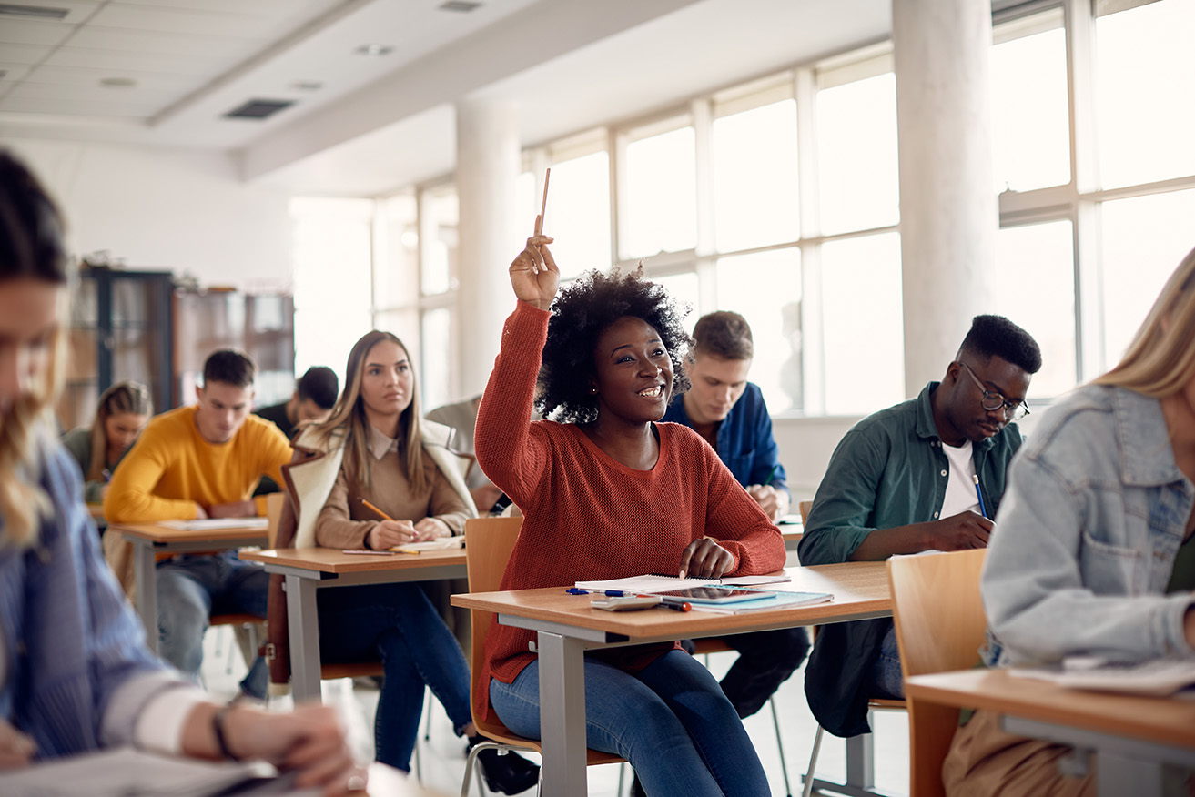 Student smiling and raising her hand in a classroom with other students